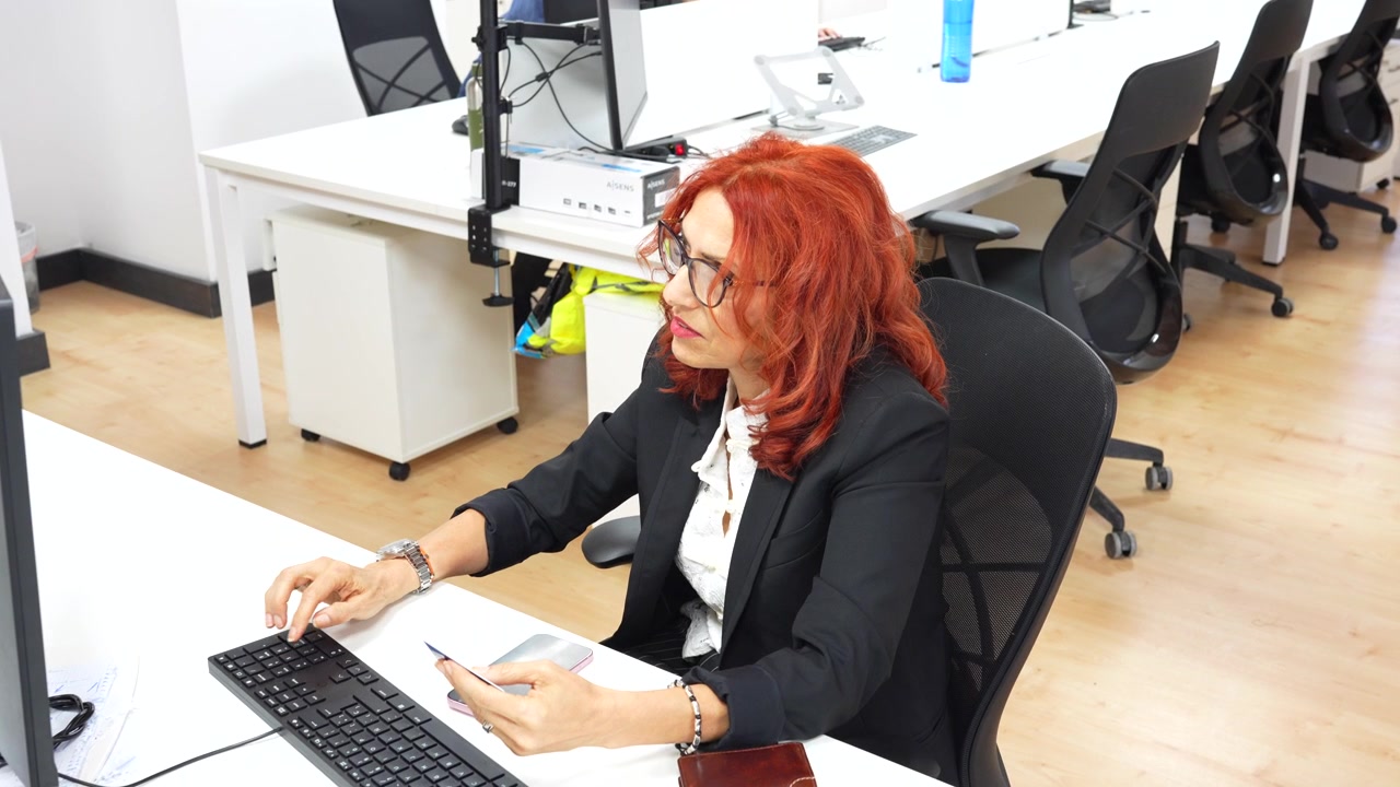 Vista de cima de uma mulher profissional com cabelo ruivo usando um computador e um smartphone em sua mesa.