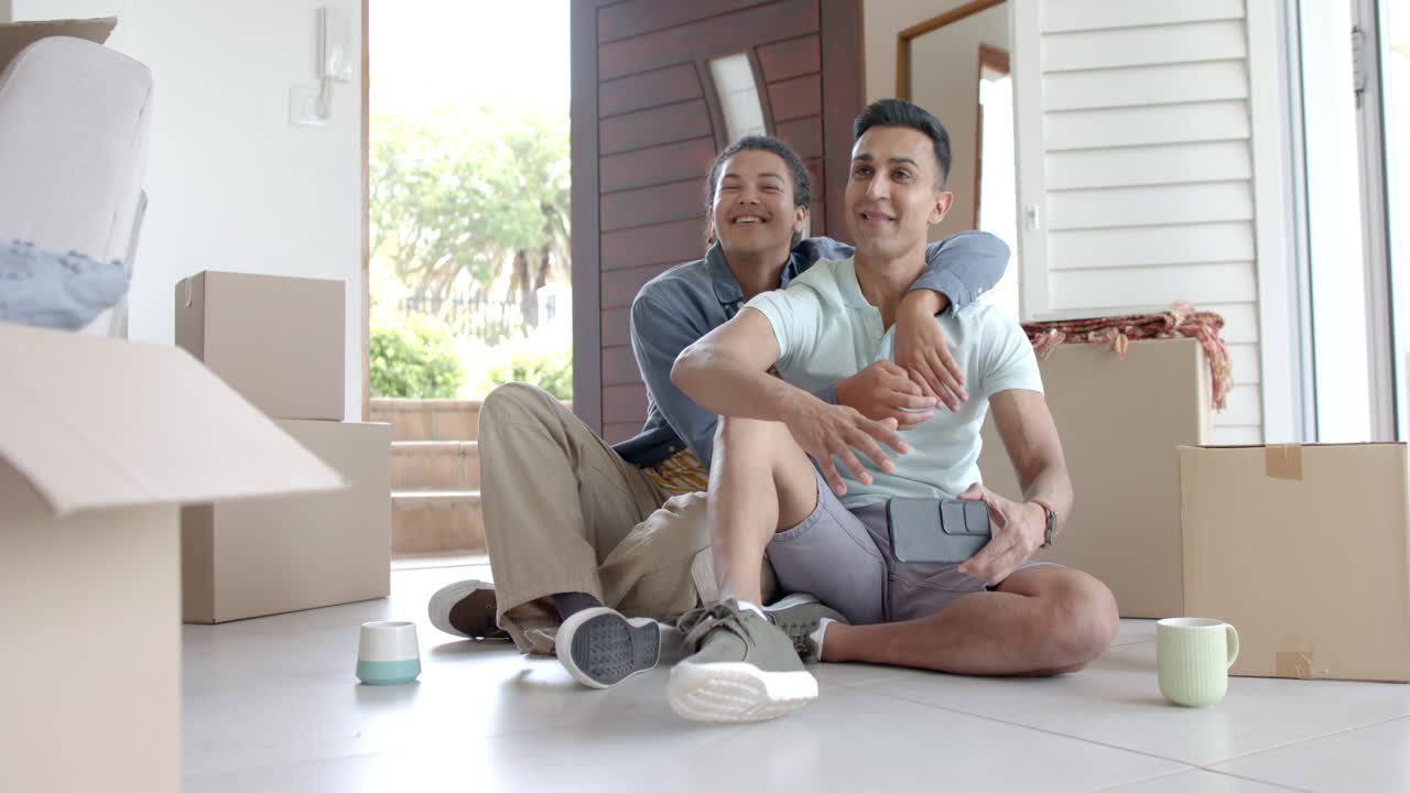 Felice coppia gay maschile di diverse etnie che si trasferisce nella nuova casa e si scatta un selfie, spazio per il testo, al rallentatore