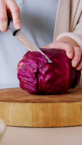 sección media de una mujer cortando repollo rojo en la cocina