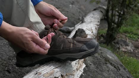 hiker tying hiking shoe laces on top of fallen tree