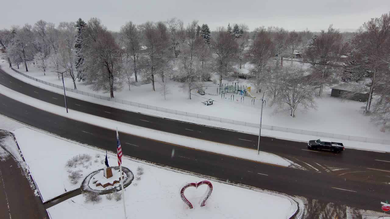 A drone flies backward through a heart shaped sculpture to reveal Loveland Colorado covered in snow