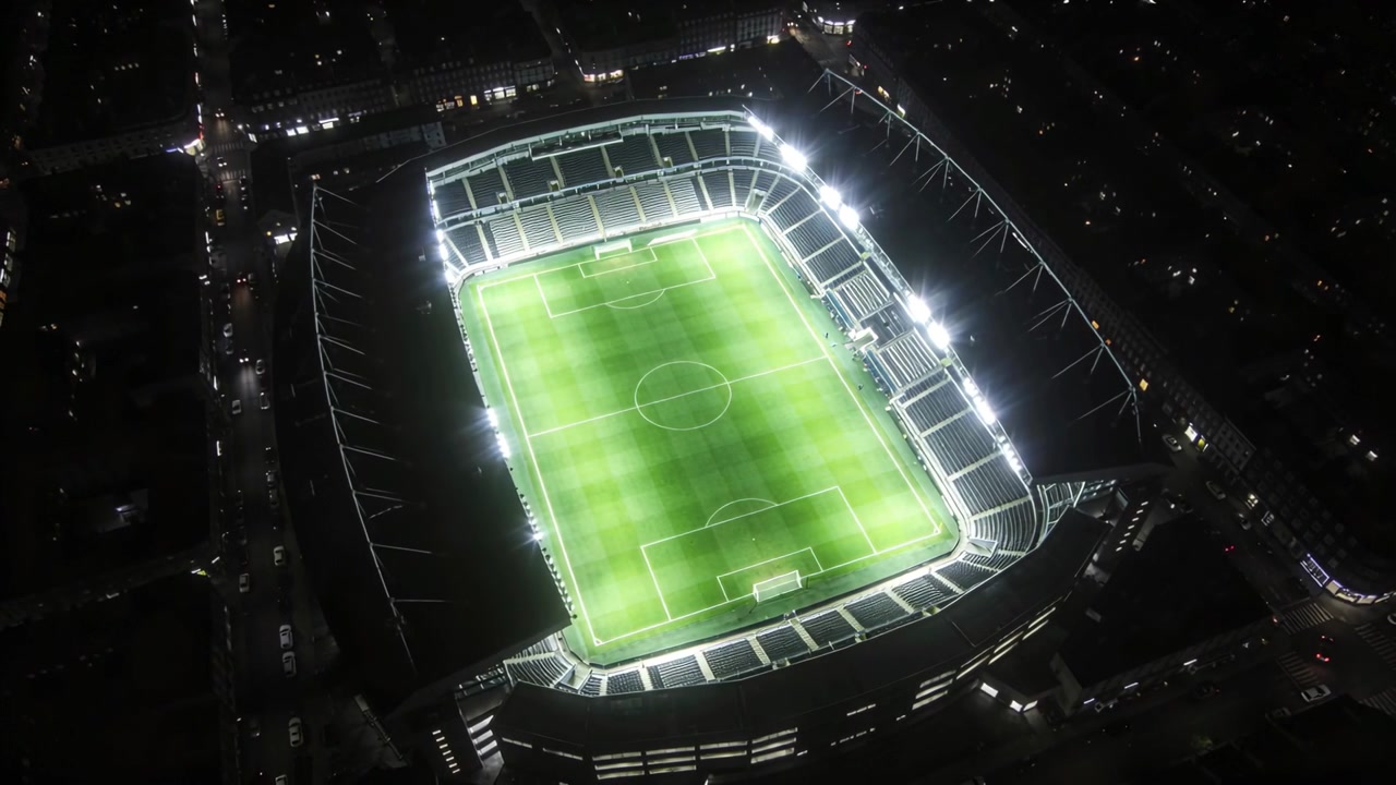 Drone che inizia a ruotare, rivelando uno stadio di calcio illuminato di notte, mostrando luci e campo segnato.