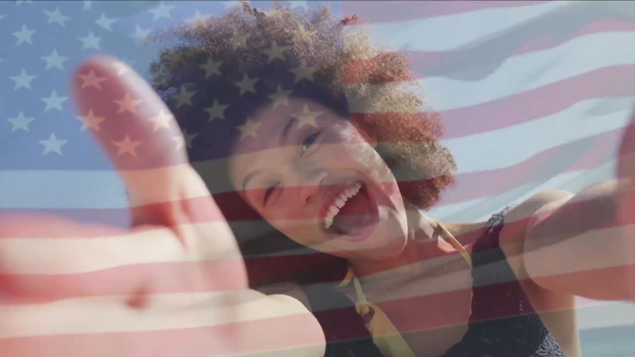 Animation of flag of united states of america over happy african american woman on beach