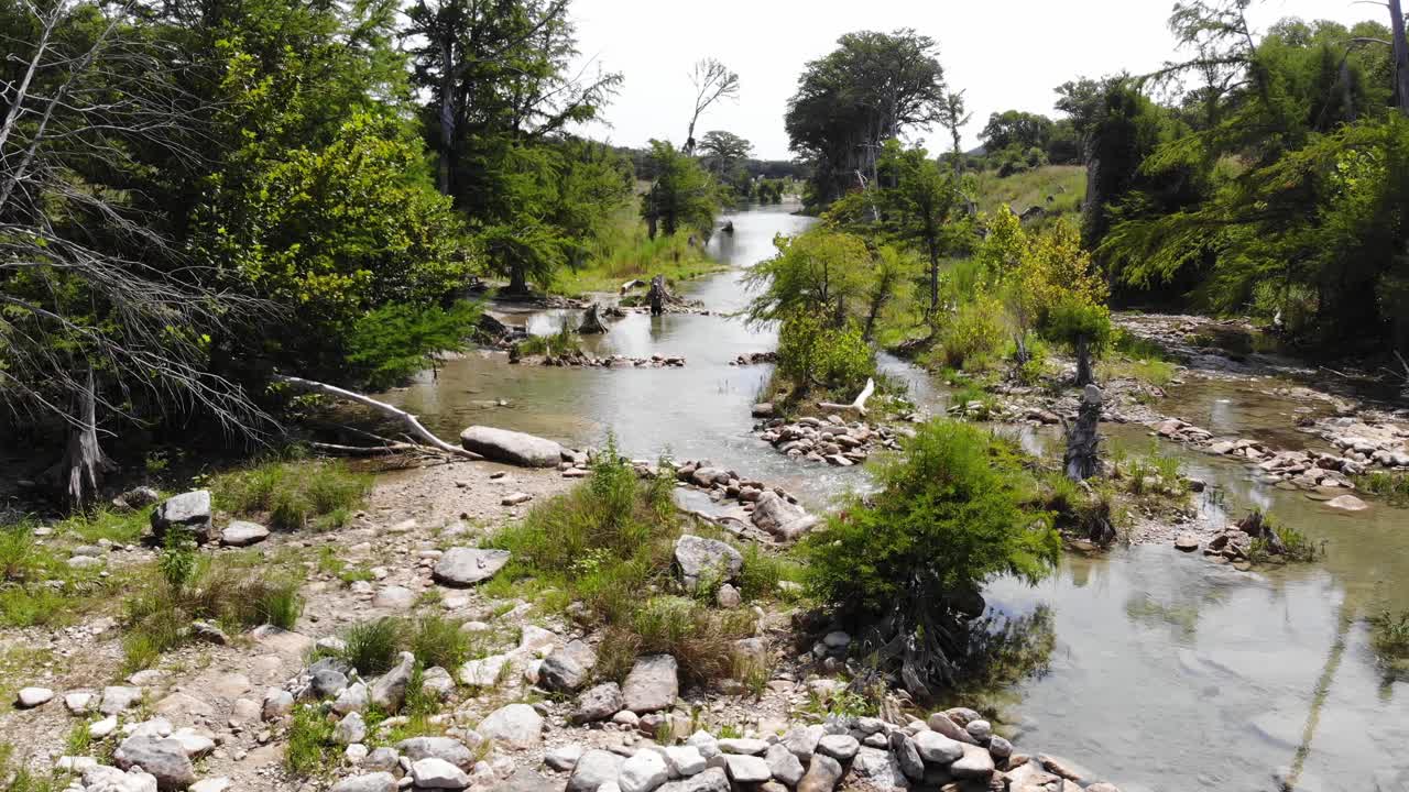 volando lentamente sobre una zona de baño hecha por el hombre con muchas rocas, árboles y el río cortando entre ellos