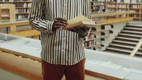 Midsection-of-Black-Man-Reading-Book-in-Library