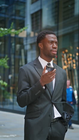 vertical video shot of young businessman wearing suit talking on mobile phone using built in microphone standing outside offices in the financial district of the city of london uk shot in real time 1