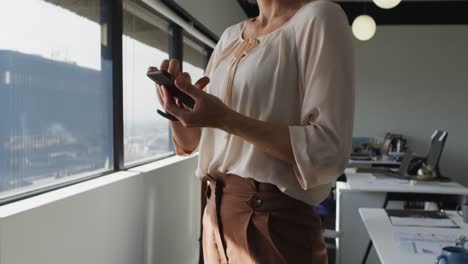 Sección-Media-De-Una-Mujer-De-Negocios-Caucásica-De-Pie-Y-Usando-Un-Teléfono-Inteligente