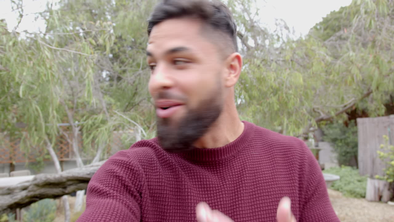 Smiling man talking on video call on phone in backyard garden, enjoying nature, copy space