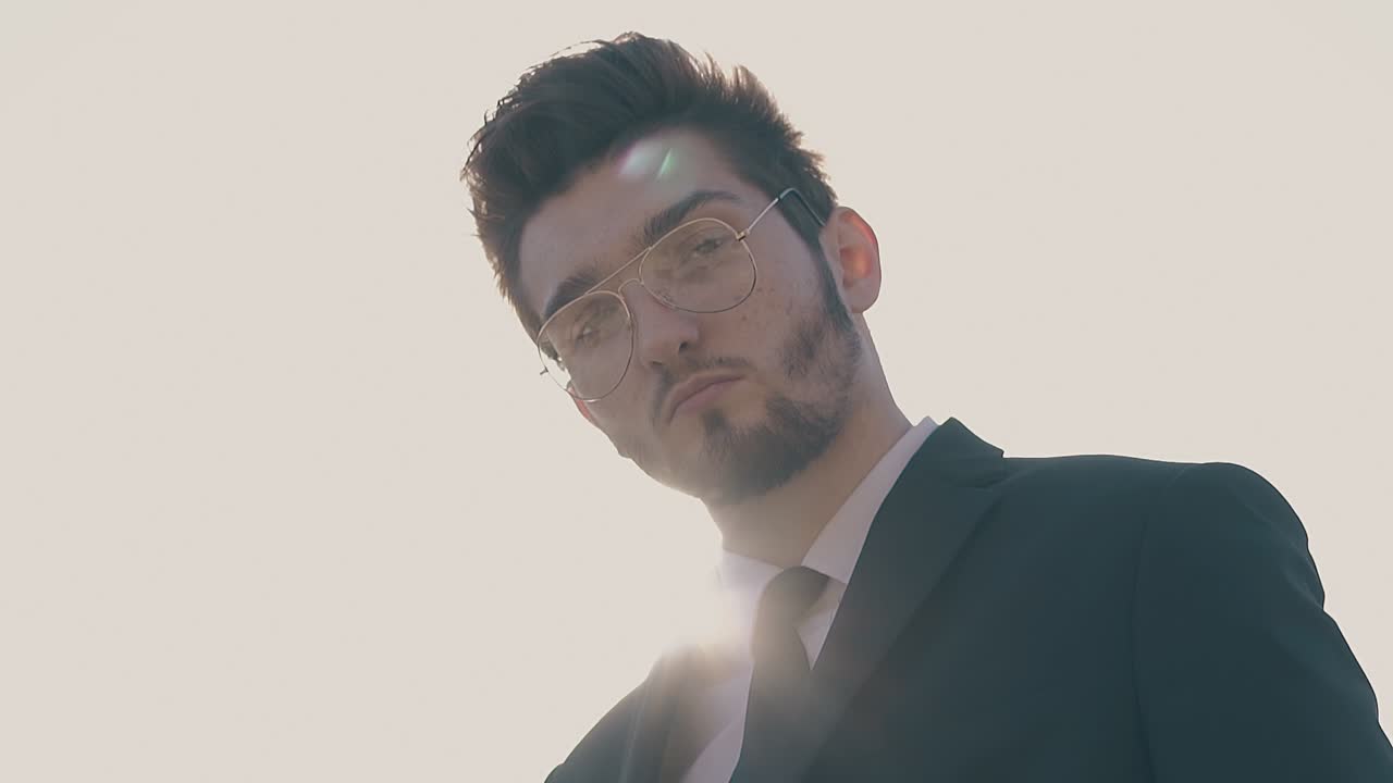 un joven barbudo con gafas se para contra el cielo en cámara lenta