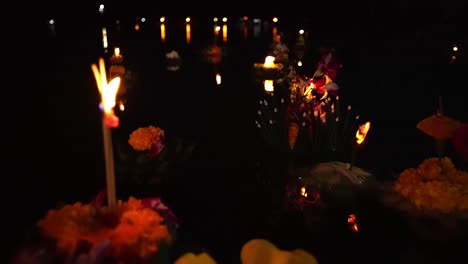 dozens of beautifully decorated baskets called krathongs, float on the surface a lake at night with lit candles during the loy krathong festival in thailand