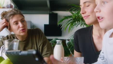 lesbian mothers and kid using tablet and chatting on breakfast