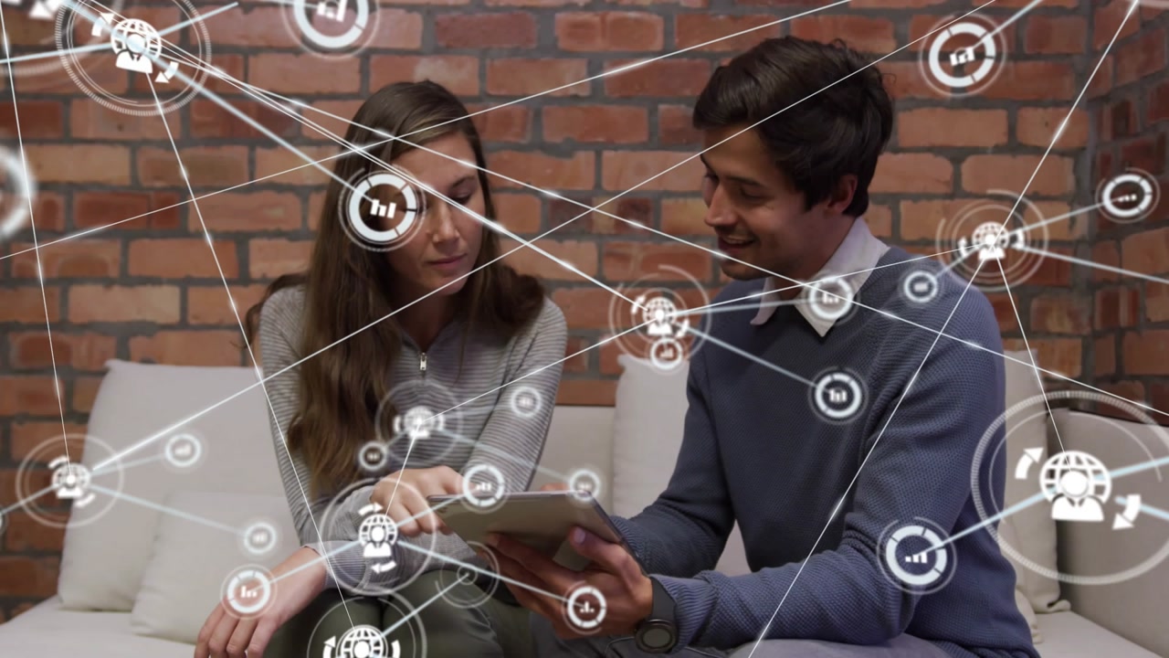 Vertical video: Tapping tablet pair in casuals collaborating on sofa by brick wall, growing overlay