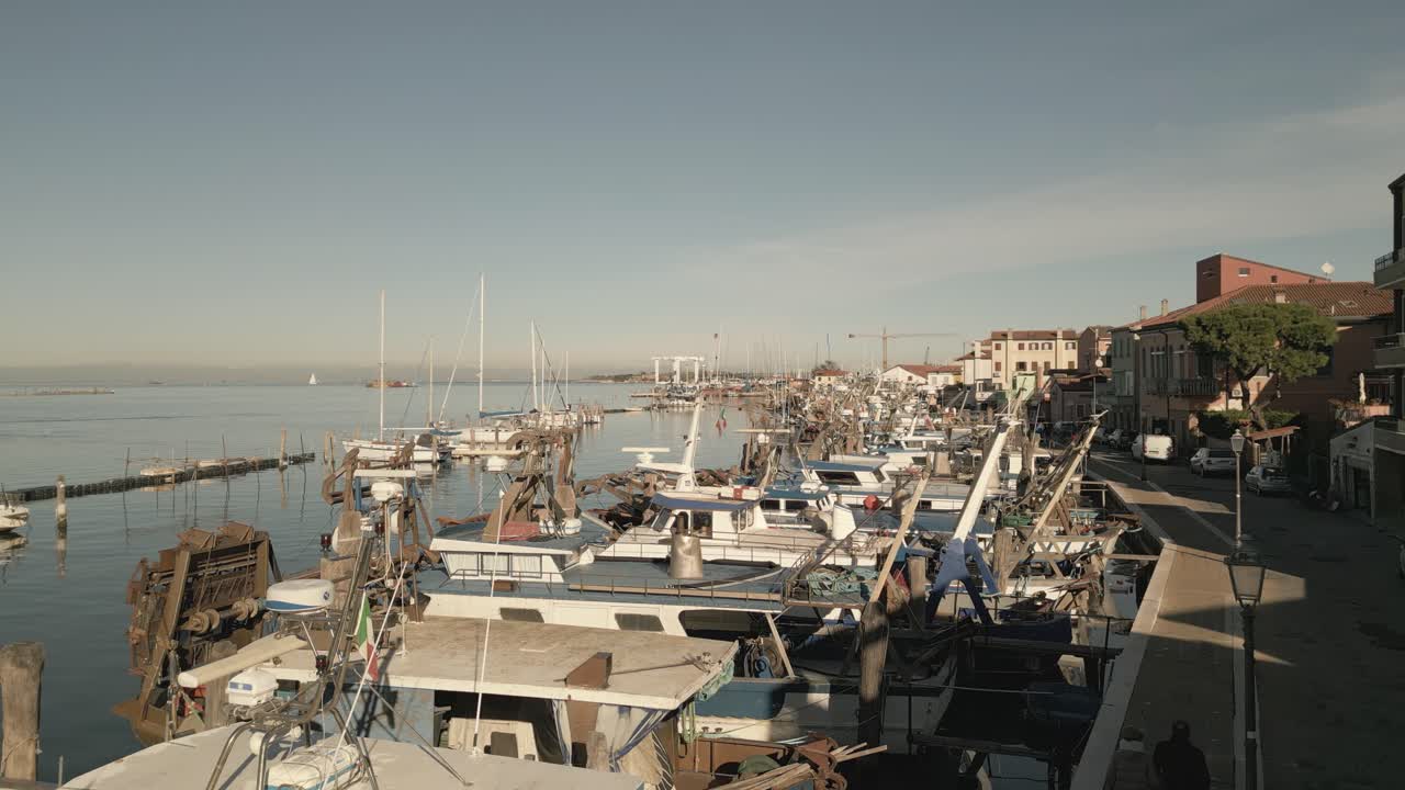 Un drone scende verso la banchina del porto turistico con barche ormeggiate e le acque calme del porto.