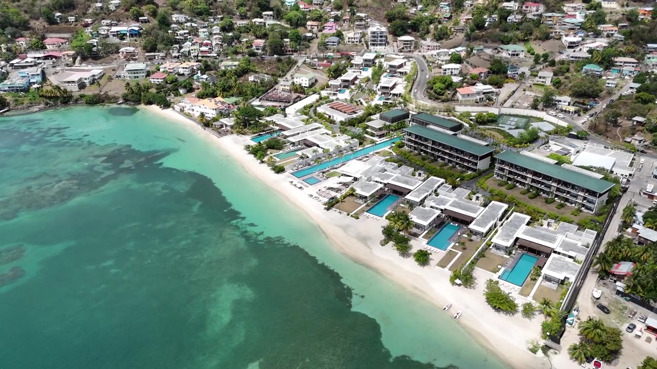 Ampia ripresa aerea con drone di lussuose proprietà di resort costieri lungo la costa di sabbia bianca di Grand Anse Beach, con carrellata sulle acque tropicali poco profonde a Grenada, Caraibi.