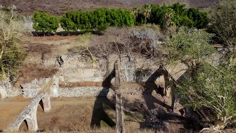 dolly in drone flight over ex hacienda san jacinto ixtoluca ruins, la mezquitera, morelos. overhead view of large stone ruins with arches and open walls surrounded by dry trees and greenery.