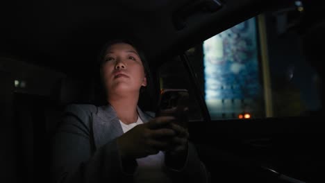 business chinese woman driving in a taxi and browsing phone at nigh