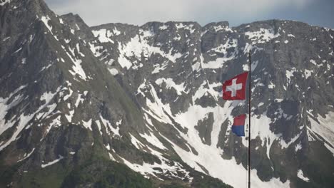 Statische-Aufnahme-Der-Flagge-Der-Schweiz-Und-Des-Kantons-Tessin,-Die-Vor-Den-Schneebedeckten-Alpen-Weht