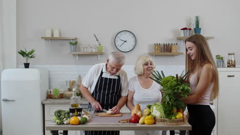 senior couple in kitchen receiving vegetables from granddaughter. healthy raw food nutrition