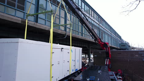 two cranes holding up big air conditioning unit, prepared for installation on top of building in brooklyn, new york usa, drone shot