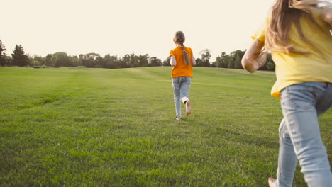 back view of two little sisters running barefoot on meadow in the park