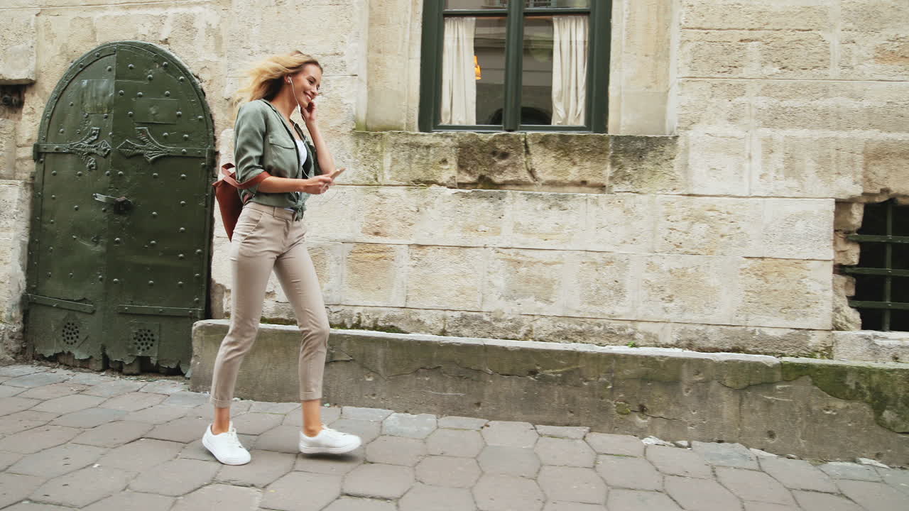 Caucasian blonde young woman walking down the street while jumping and listening to music