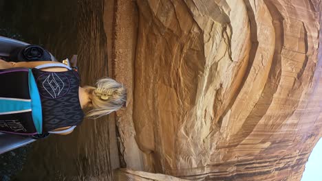 Vertical-POV-shot-of-a-blondwoman-sailing-on-a-waterscooter-next-to-the-high-rocks-at-Lake-Powell