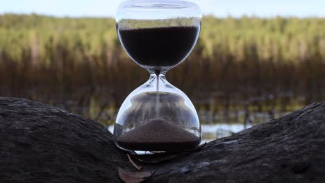 peaceful unsharp lake and forest in background and sharp old style time glass on the rock