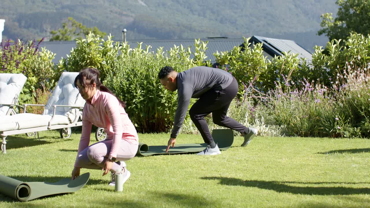 Pasangan Afrika-Amerika dengan pakaian olahraga memasuki halaman membawa tikar yang digulung, membentangkan tikar untuk yoga.