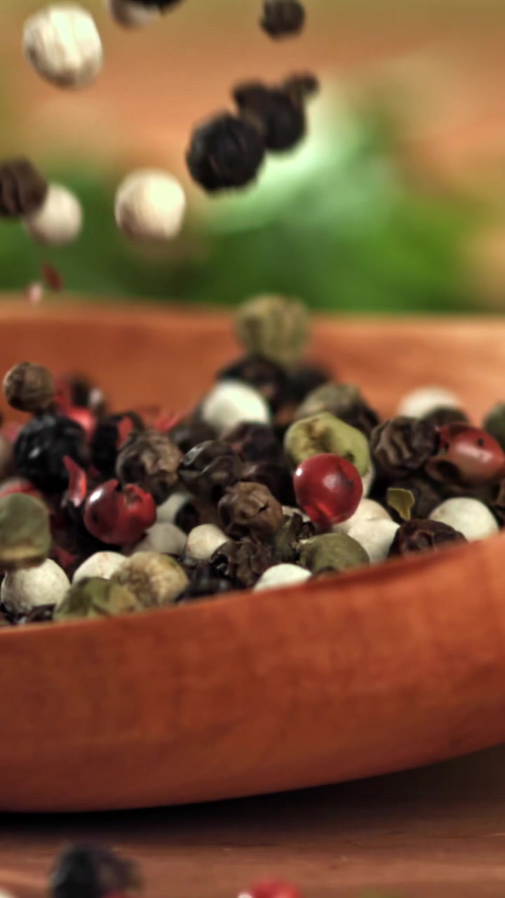 Assorted Peppercorns Falling into a Wooden Bowl in Slow Motion