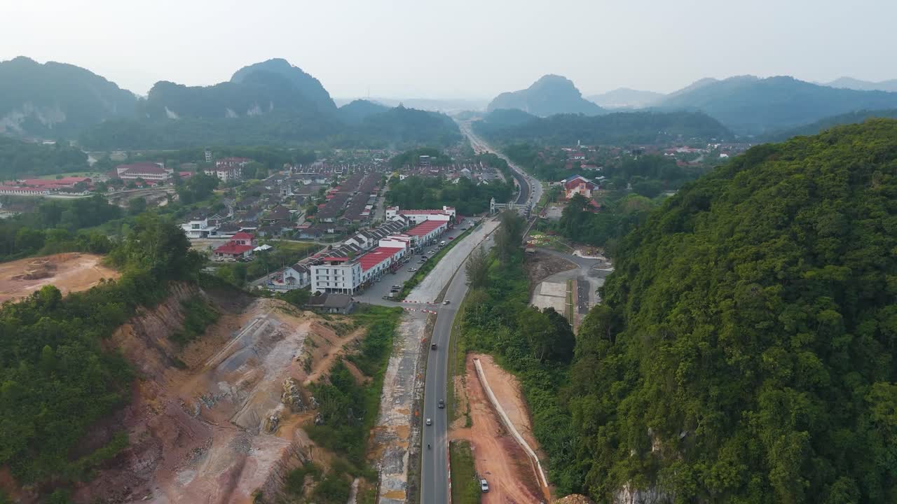 Push-in aerial shot of Gua Musang, Kelantan, Malaysia, featuring a highway cutting through lush greenery with dramatic limestone hills rising in the background