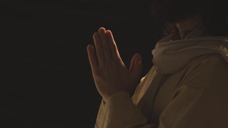 close up of man wearing robes with long hair and beard representing figure of jesus christ putting hands together in prayer 1