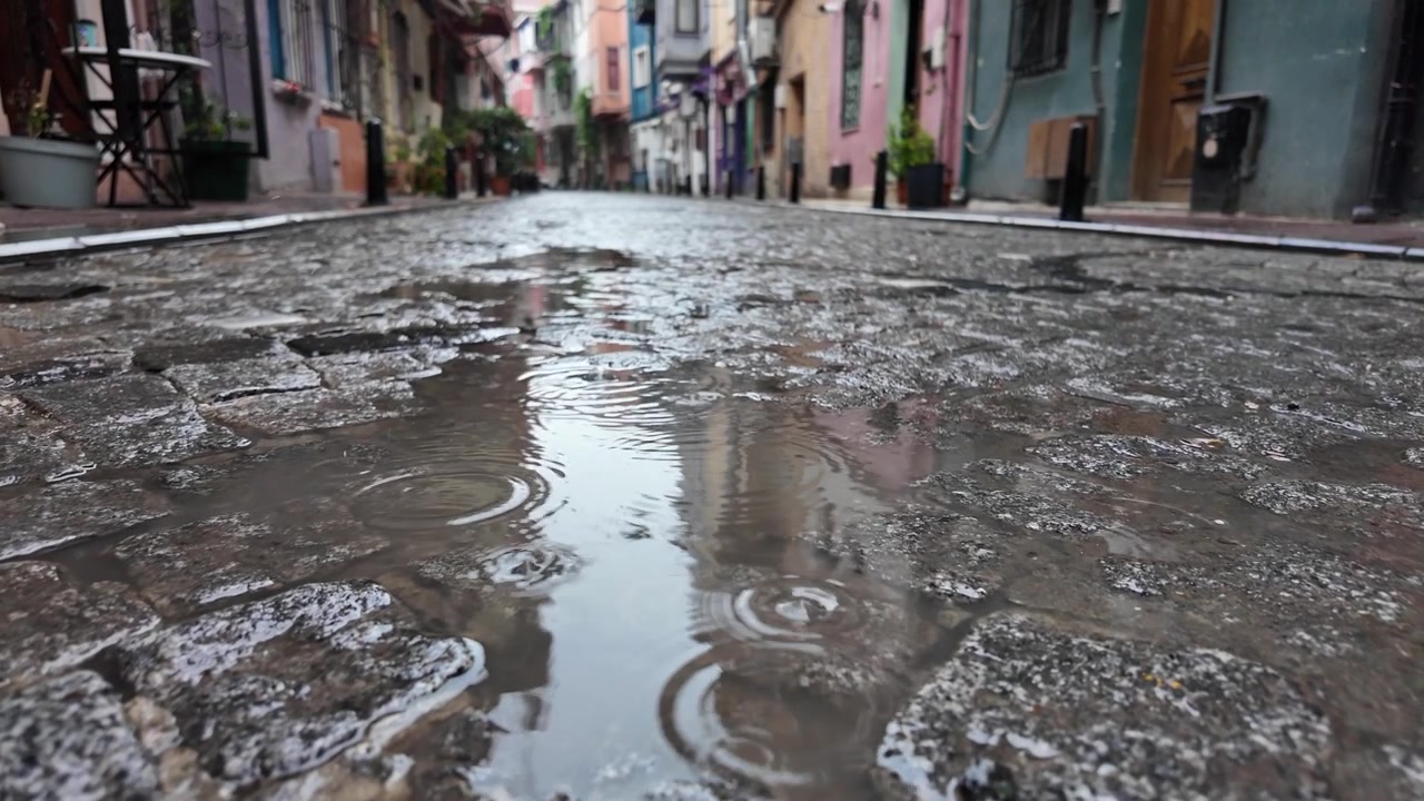 Gocce di pioggia che cadono in una pozzanghera su una strada di ciottoli.