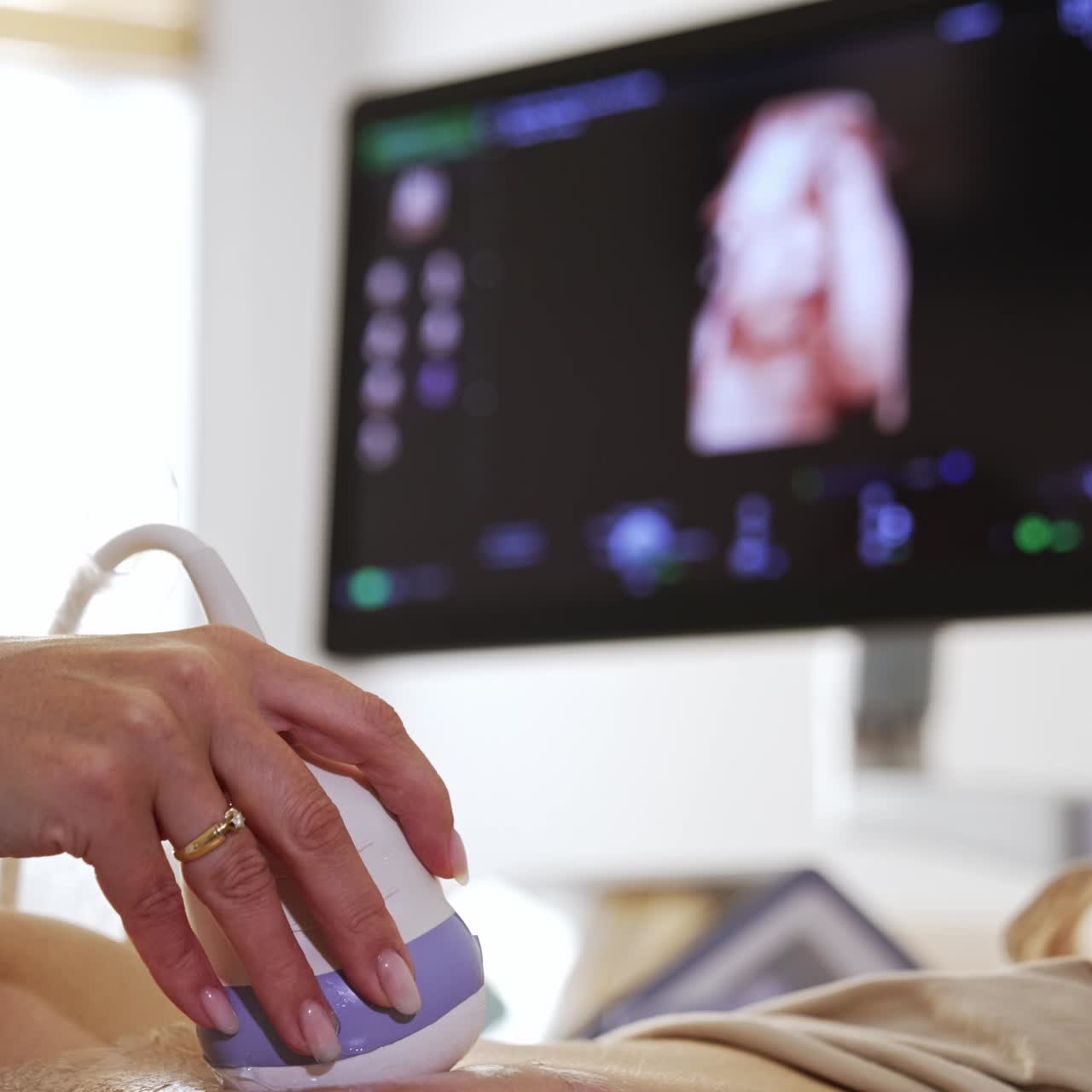 Doctor carrying out the ultrasonic check to a patient. Physician's hand holding the transducer from machine on the female belly covered with gel. Blurred backdrop