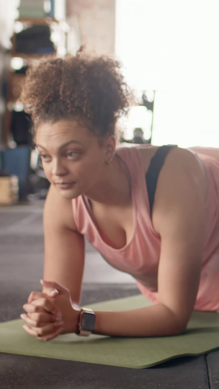 Video verticale: Donna che inizia a fare il plank sugli avambracci su un tappetino verde in palestra, con una canotta rosa per il fitness.