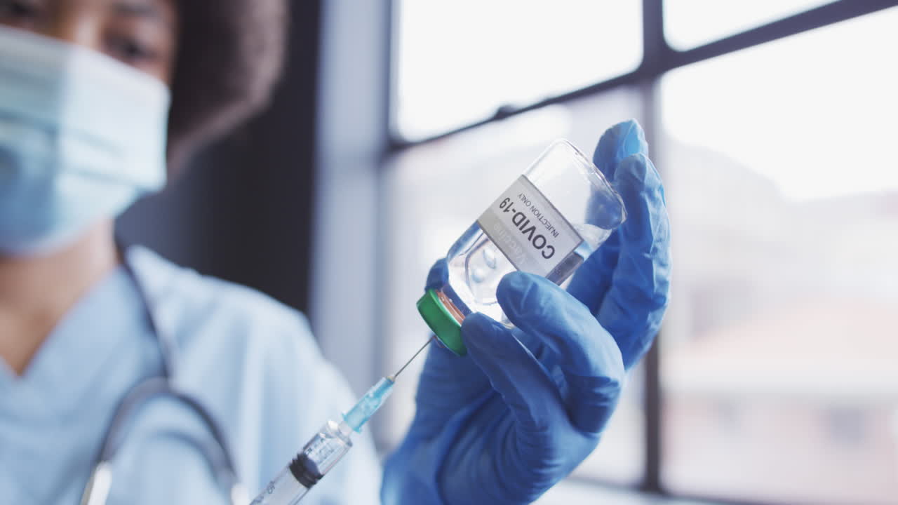 doctora de dos razas con máscara facial llenando una jeringa