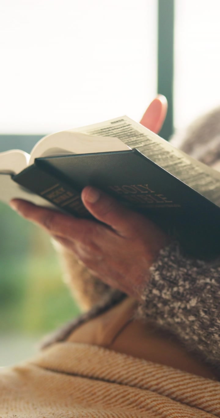 Person Reading a Holy Bible While Relaxing Indoors