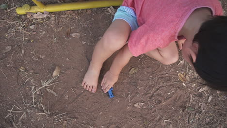 Slow-Motion-high-angle-crane-clip-of-an-East-Asian-boy-kid-enjoying-playing-with-toy-truck-sitting-on-the-floor-of-an-outdoor-playground-with-toy-cars-and-going-down-the-slider-after-school