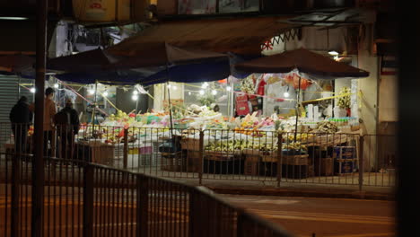 Static-shot-of-people-walking-through-a-local-fruit-and-vegetable-shop-and-a-bus-appearing-in-view