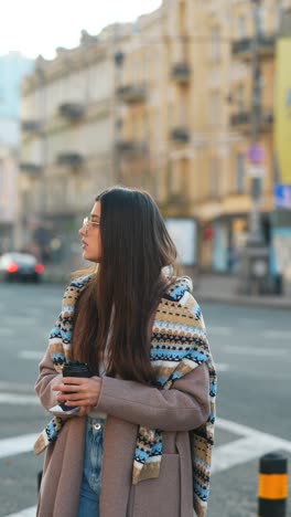 young woman walking in city street with coffee and phone