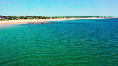 aerial drone video of busy beaches in saco, maine, during peak summer. crowds relax on sandy shores near vacation homes as atlantic ocean waves crash along the lively coastline.
