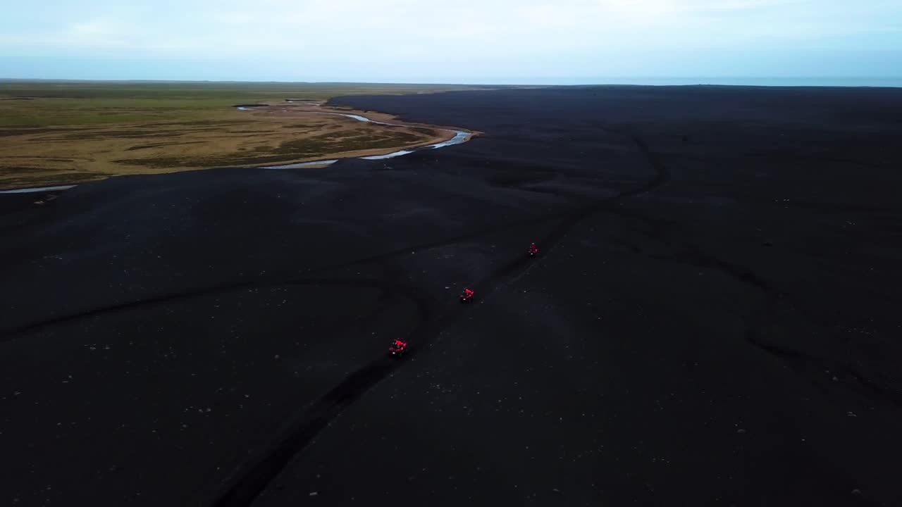 Aerial view of bright red quad bikes speeding off road through Iceland black sand beach