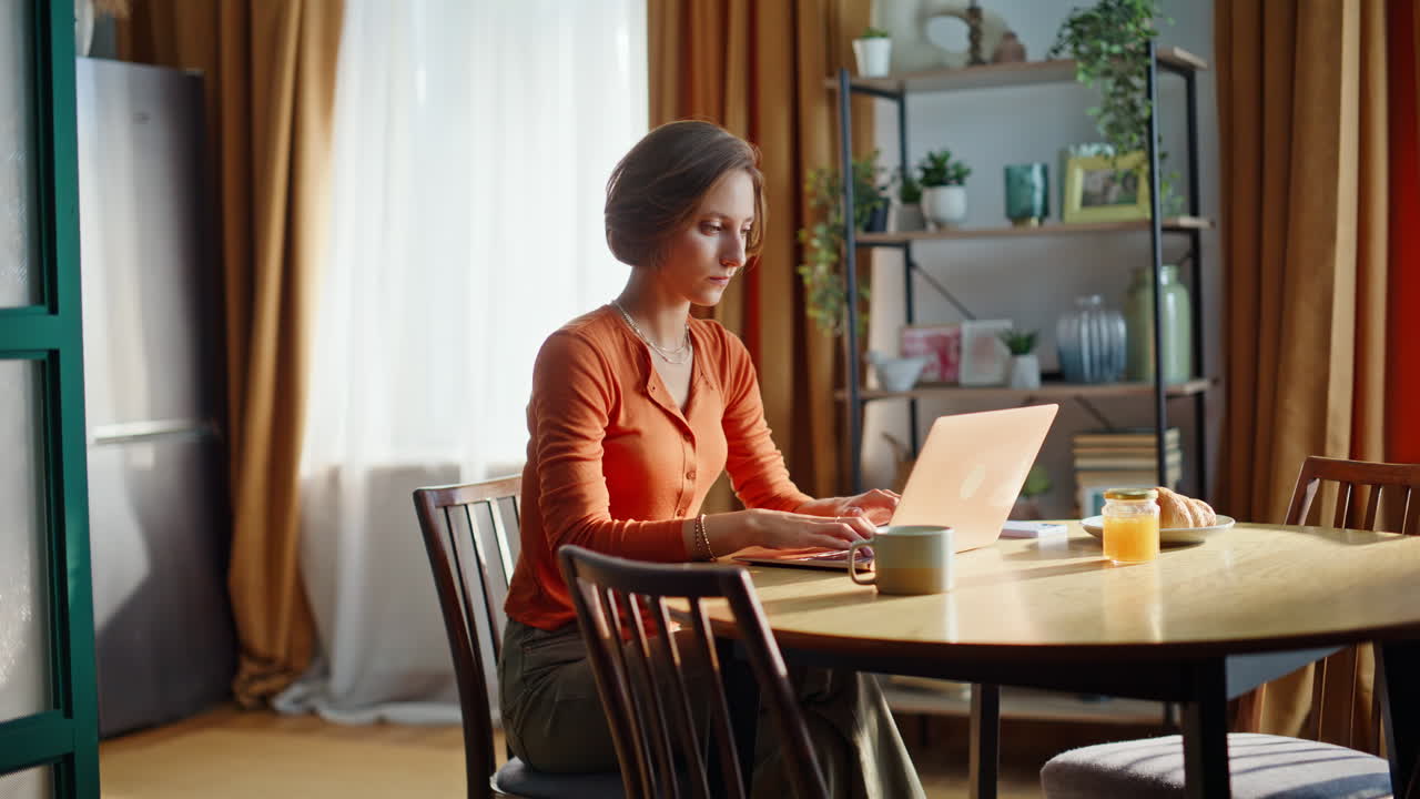 Pensive freelancer working project sitting apartment kitchen. Woman typing home