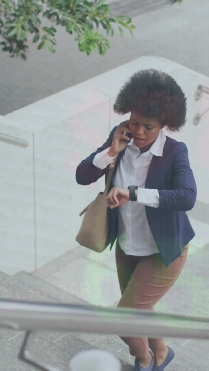 Animation of numbers over african american woman checking time and talking on phone walking on steps