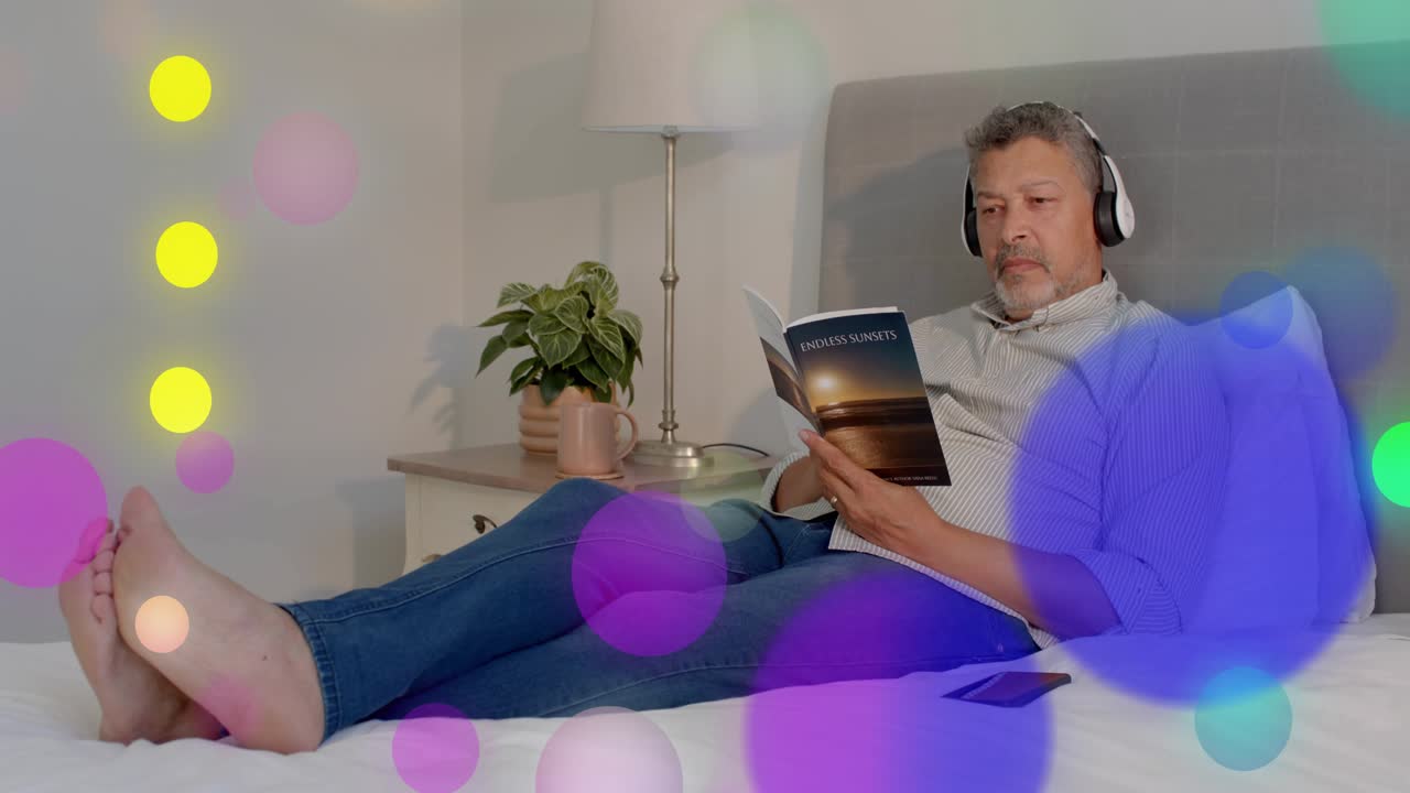 Man glancing lying on bed, reading and turning pages, pausing while bokeh obscuring lifestyle