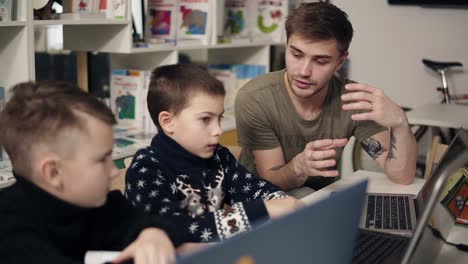 un joven y atractivo profesor de programación está explicando algo sobre tecnologías y computadoras a sus dos alumnos. proceso educativo.