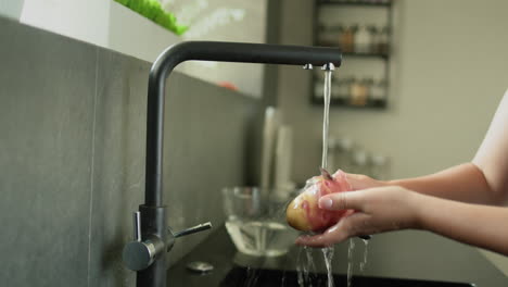 una mujer pelando patatas bajo el agua corriente de un grifo de la cocina.