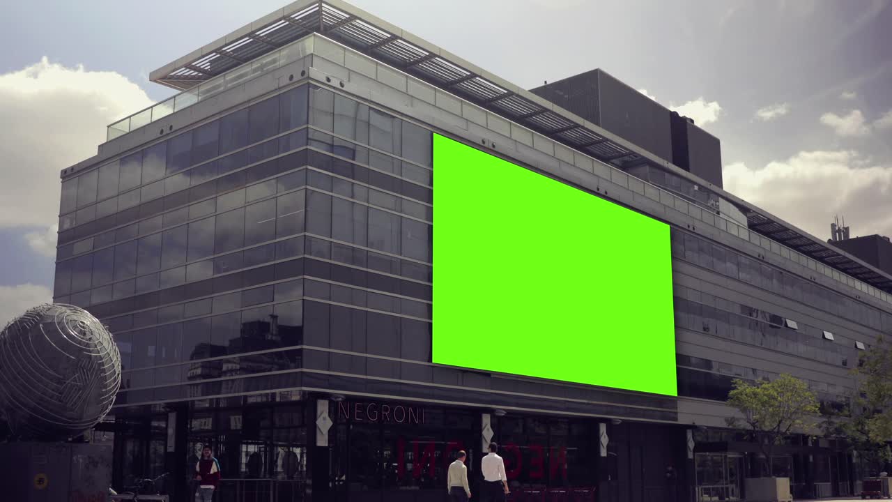 Cartellone green screen sull'esterno di un moderno edificio cittadino con pedoni.