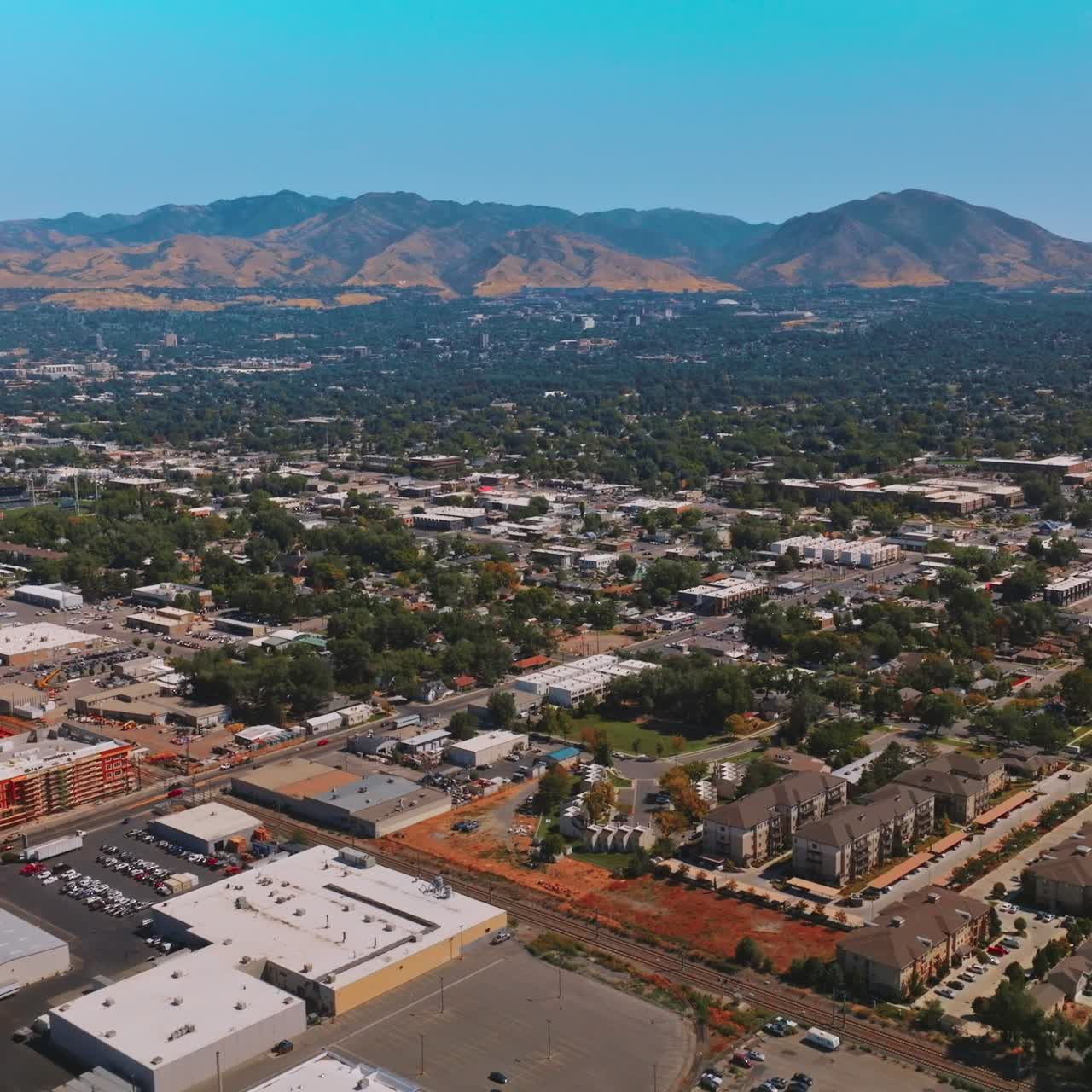 Picturesque green panorama of Salt Lake City on sunny hot day. Mountainous skyline at backdrop. Aerial view
