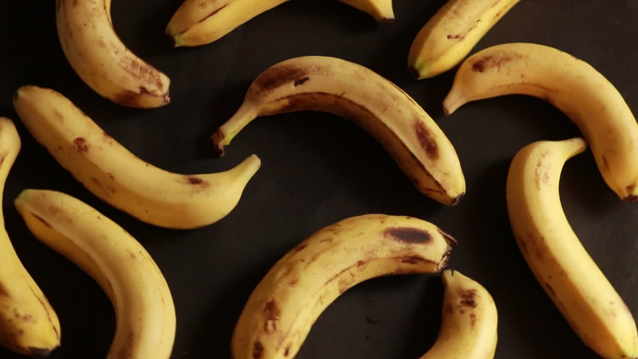 plátanos húmedos deliciosos maduros giran en el sentido de las agujas del reloj sobre un plato negro sobre un fondo negro