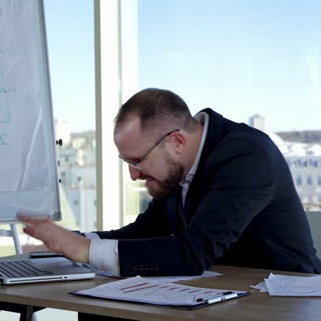 Funny businessman typing on a laptop. Office worker in glasses sitting at his desk in workplace and making mad face. Problems in business